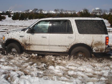 2002 Ford Expedition - A white SUV is stuck in a muddy, snowy area, with its wheels deep in the muck.