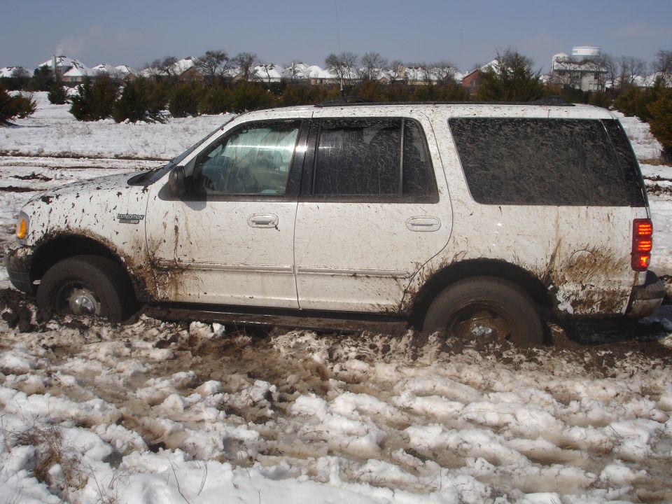 White SUV stuck in mud and snow. The vehicle appears to be a 2002 Ford Expedition