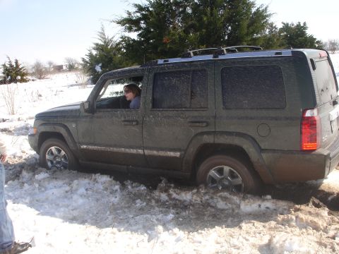 2002 Ford Expedition - A dark green Jeep Commander is stuck in the snow, with its tires partially submerged in mud and snow.