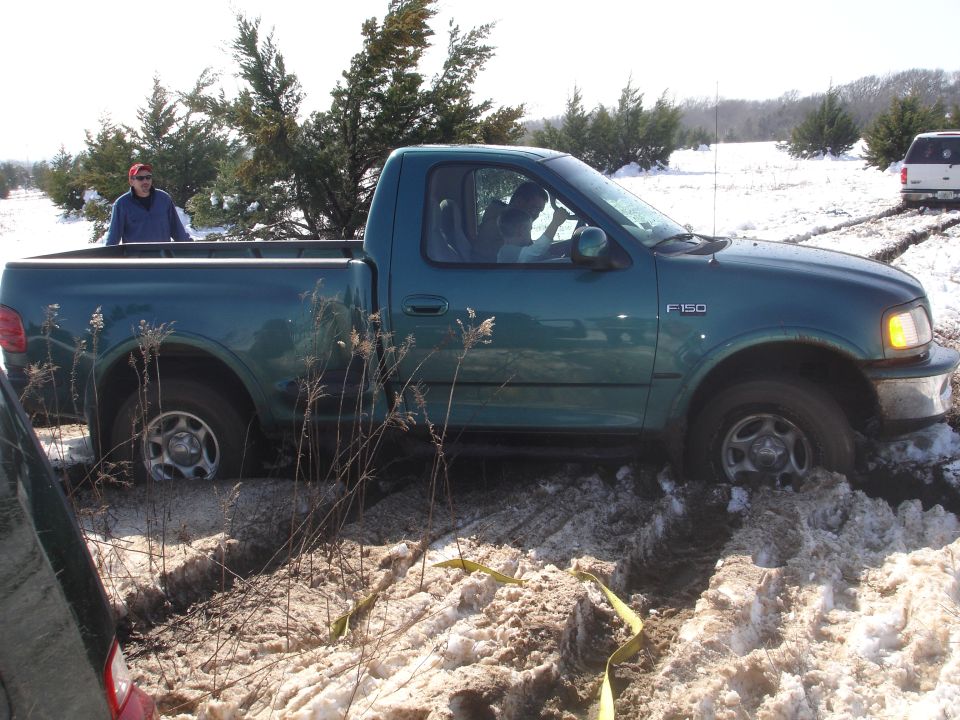 Green Ford F-150 stuck in snow, with another vehicle visible in the background