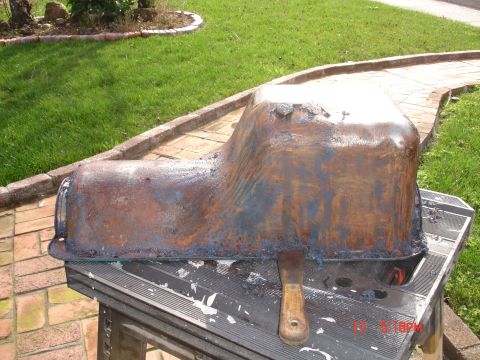 1978 Ford Mustang II - A rusty oil pan is being cleaned on a portable workbench outdoors.