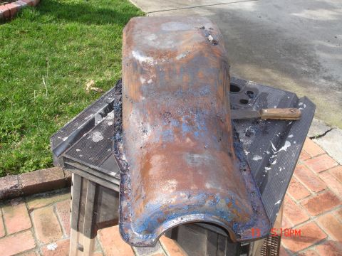 1978 Ford Mustang II - A heavily rusted car fender sits on a sawhorse outdoors.