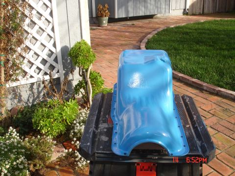 1978 Ford Mustang II - A bright blue oil pan sits on a black stand outdoors, with a brick walkway and green grass visible.