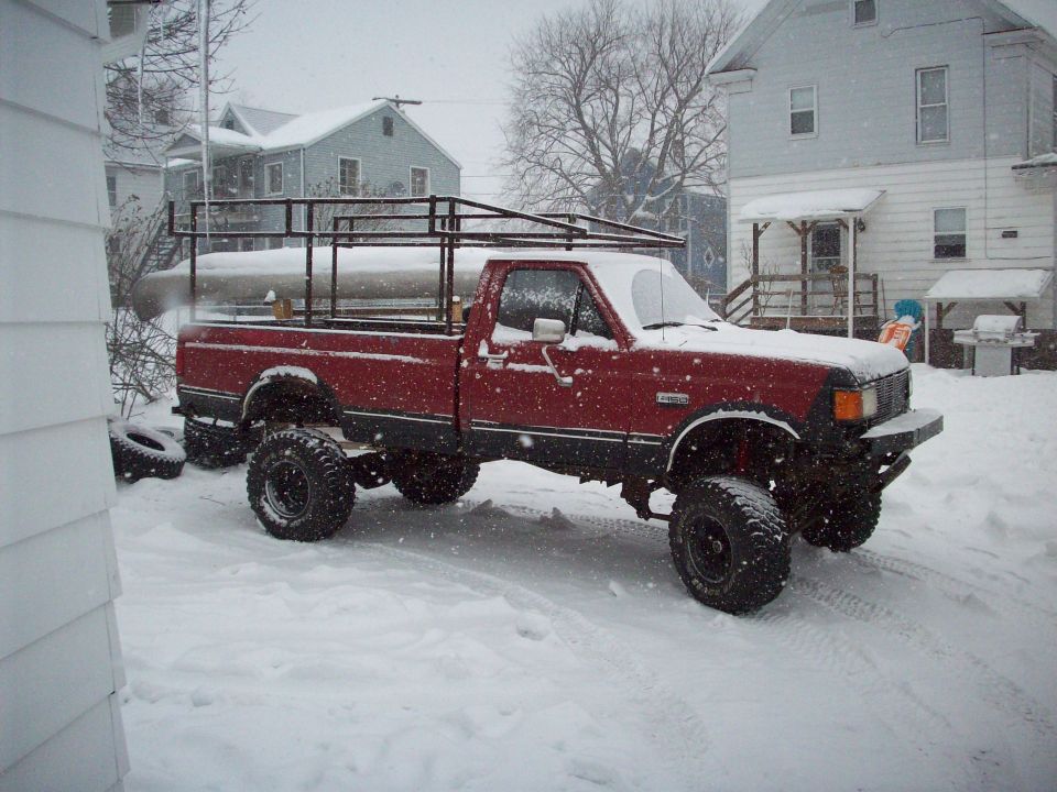 Red lifted Ford pickup with bed rack in a snowy driveway