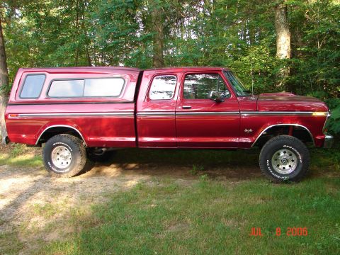 1979 Ford F-150 - This red 1979 Ford F-150 Supercab pickup truck is shown in a side profile, equipped with a camper shell and lifted suspension.