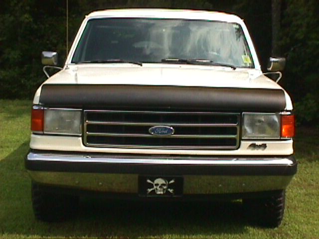 Front of a white 1980s Ford 4x4 truck with chrome grille, Ford oval and skull-and-crossbones front plate on grass