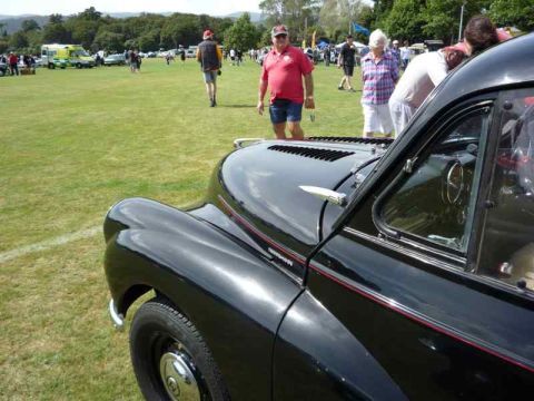 1969 MINI Cooper - A black classic car is displayed at an outdoor event with other vehicles and people in the background.