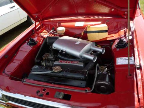 1969 MINI Cooper - Engine bay view of a red car, a LOTUS valve cover and a large muffler with dual outlets.