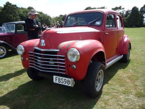 1969 MINI Cooper - A classic red car with a distinctive grille is parked on a grassy field, with another vehicle nearby.