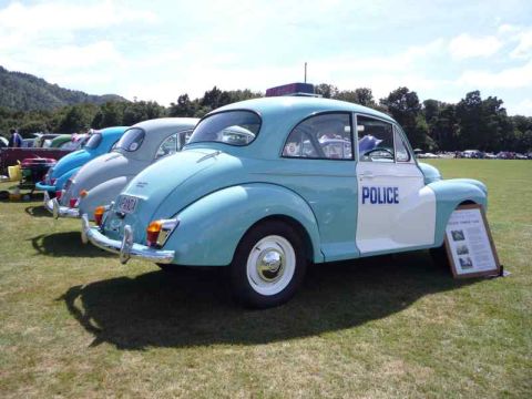 1969 MINI Cooper - A light blue and white police car is parked on a grassy field with other vehicles in the background.