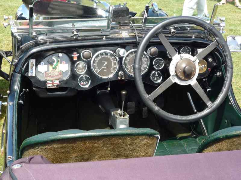 Dashboard of a vintage car, showing gauges, steering wheel, and green seats. Watermark 'SUPERMOTORS www.supermotors.net' visible