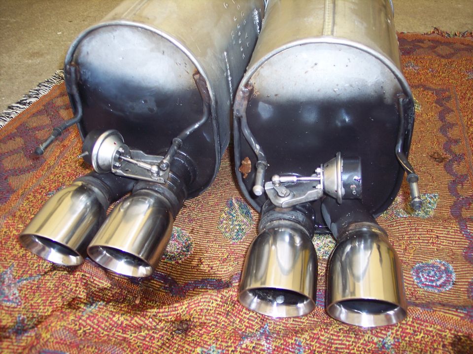 Pair of chrome exhaust tips with active exhaust valves, resting on a patterned rug
