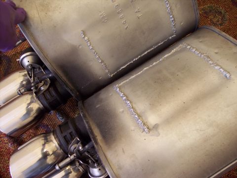 2006 Chevrolet Corvette - Close-up of exhaust mufflers, one shows GM part number 89068 stamped on it.