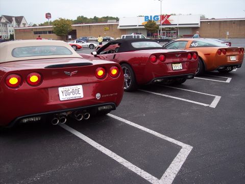 2006 Chevrolet Corvette - Three Corvettes parked in a lot, two red convertibles and one orange coupe.