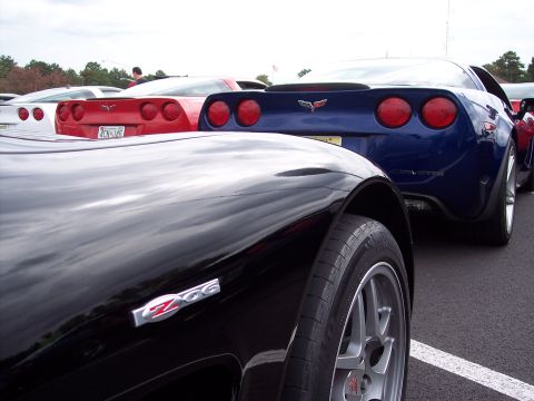 2006 Chevrolet Corvette - Multiple Chevrolet Corvettes, including a black Z06 and a blue model, are parked in a lot.