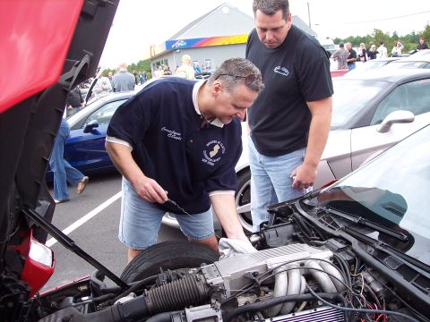2006 Chevrolet Corvette - Two men examine the engine bay of a red car during an outdoor event.