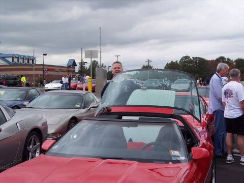 2006 Chevrolet Corvette - Multiple Chevrolet Corvettes gathered outdoors, with a man standing next to a red convertible.