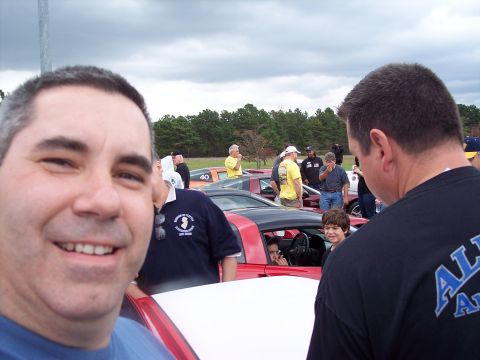 2006 Chevrolet Corvette - A group of people gathered around cars on a cloudy day.