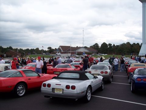 2006 Chevrolet Corvette - A gathering of Chevrolet Corvettes in a parking lot under a cloudy sky.