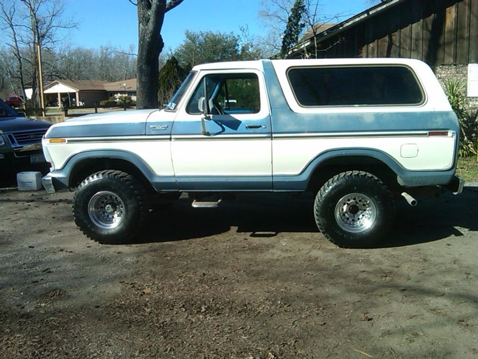 Blue and white 1978 Ford Bronco lifted on chrome wheels, side view