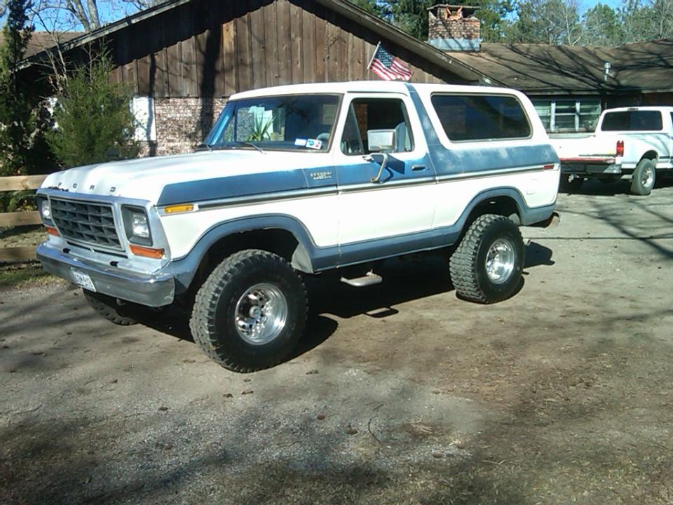 Blue and white 1978 Ford Bronco parked in front of a cabin