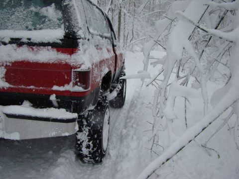 1948 Jeep Wrangler - A red pickup truck navigates a snowy path, its large tires designed for off-road conditions.