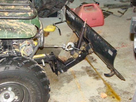 1948 Jeep Wrangler - Close-up of an ATV's front tire and a Craftsman snow plow attachment in a garage.