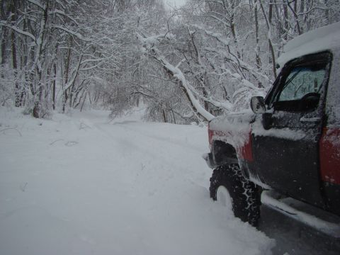 1948 Jeep Wrangler - A truck is partially buried in snow on a wintery road surrounded by snow-covered trees.