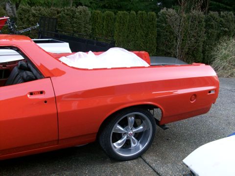 1973 Ford Ranchero - Driver-side rear quarter of a freshly painted red coupe utility during reassembly, with the door trim and bedside emblems still off and the…