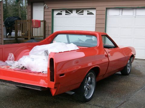 1973 Ford Ranchero - Passenger-side rear three-quarter view of a freshly painted orange-red Ford Ranchero coupe-utility on a driveway in front of white garage d…