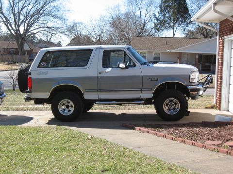 1994 Ford Bronco - This two-tone silver and white Ford Bronco is parked on a concrete driveway next to a brick garage.