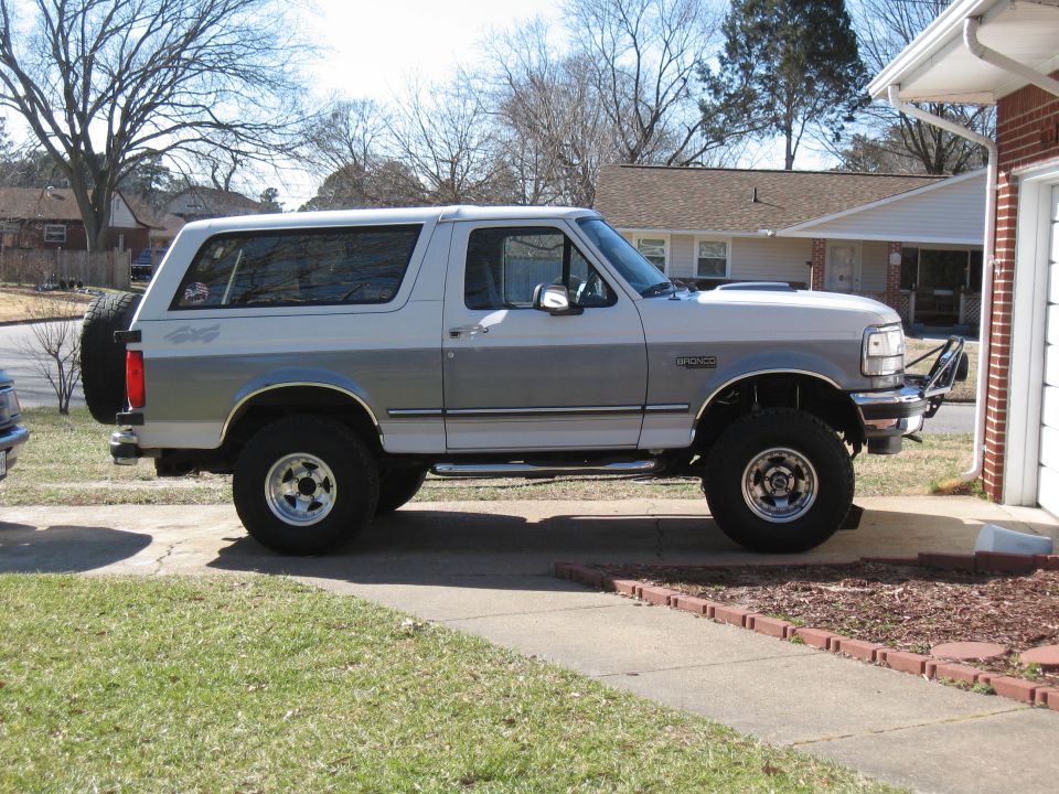 Two-tone silver and white Ford Bronco with a spare tire on the rear, parked on a driveway