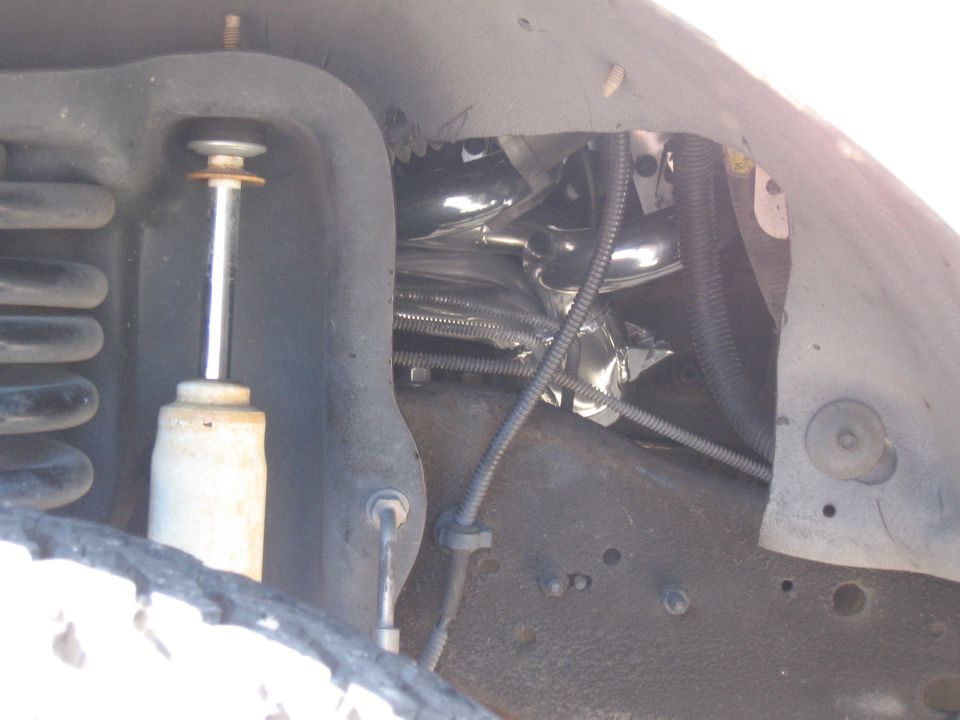 Chrome exhaust headers wrapped in heat shielding, visible near a shock absorber and coil spring