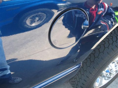 2008 Dodge 1500 - A close-up view of a blue vehicle's side, showing reflections of a person in a racing jacket and a tire on the fuel door.