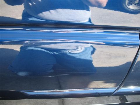 2008 Dodge 1500 - The side of a blue vehicle shows significant scratches and reflections of the surroundings.