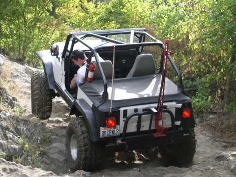 1979 Ford Bronco - White Jeep Wrangler navigates a challenging rocky off-road course with a driver inside.