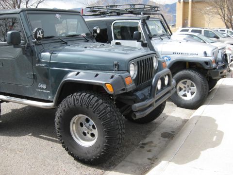 2003 Jeep TJ - Two Jeep Wranglers, one dark green and one silver, are parked next to each other on a paved surface.