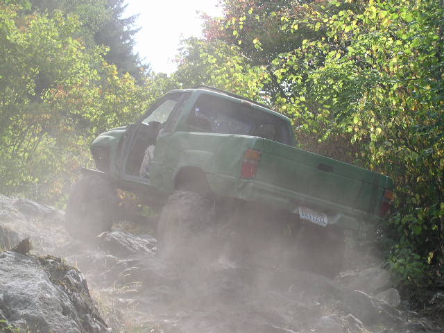Green pickup truck with large tires climbing a rocky, dusty trail