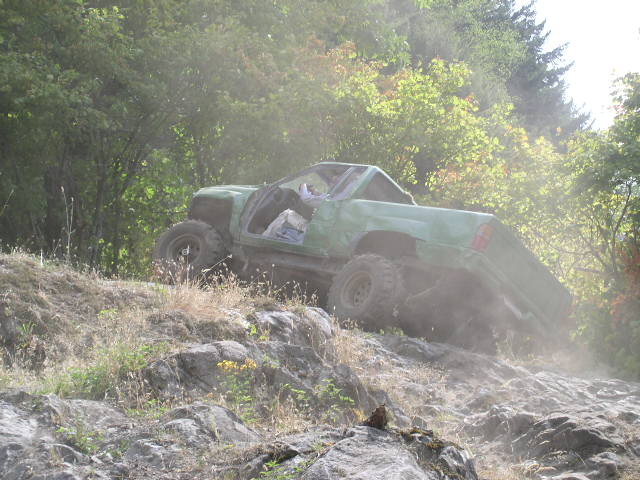 Green doorless Ford 4x4 climbing a steep rocky dirt hill with dust behind the tires