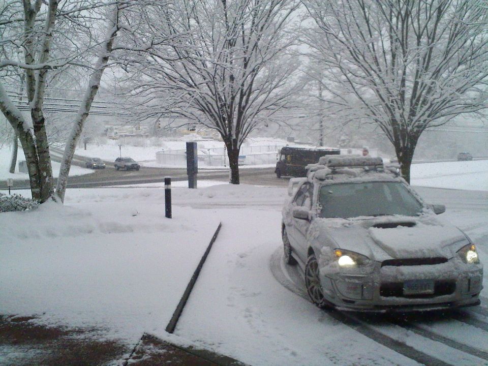 Snow-covered silver Subaru WRX wagon with hood scoop and roof rack in a snowstorm