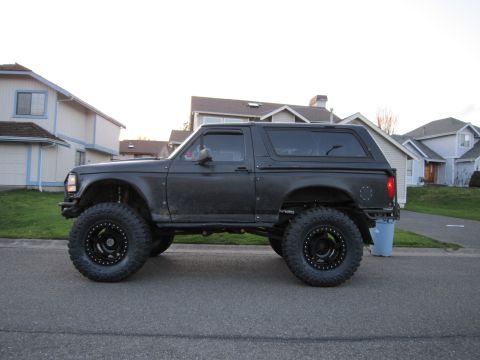 1996 Ford Bronco - Side view of a modified black Ford Bronco with oversized tires and a lifted suspension.