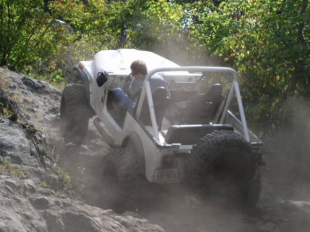 White off-road vehicle climbing a rocky hill, rear tire visible