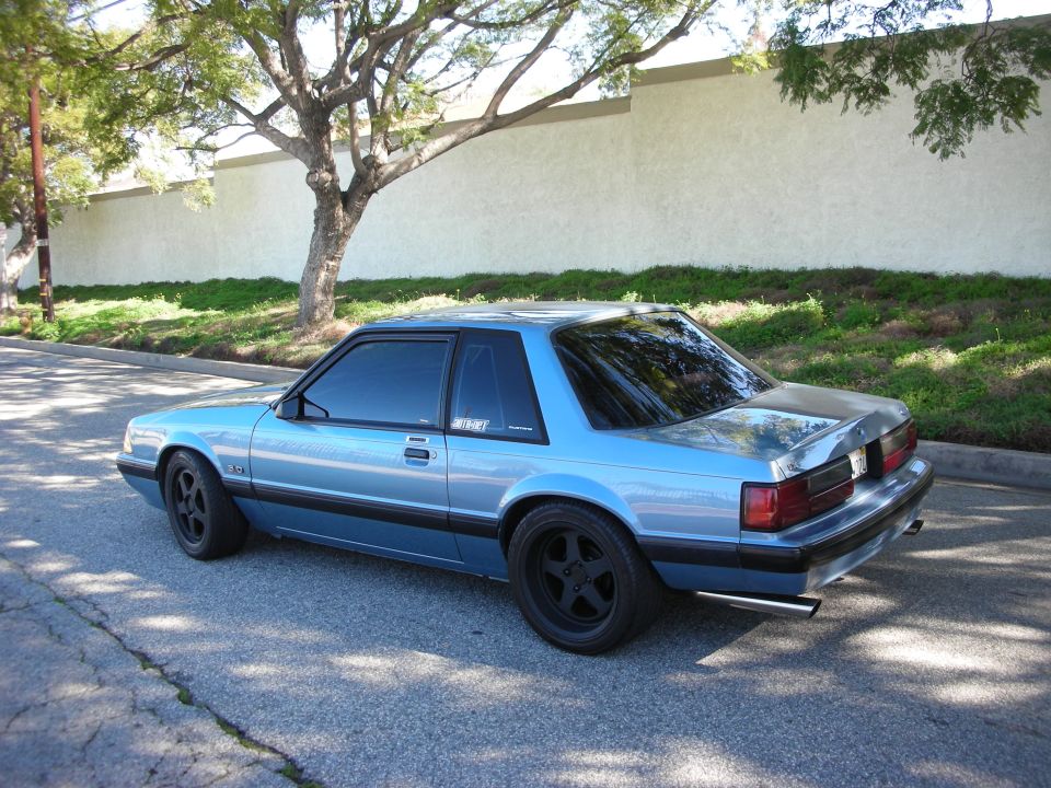 Light-blue Fox-body Mustang coupe, rear three-quarter, black wheels, dual exhaust