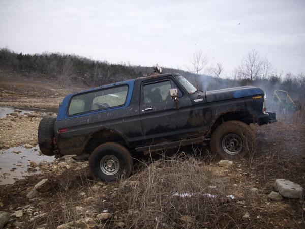 Muddy blue and black lifted Ford Bronco climbing rocks on an off-road trail
