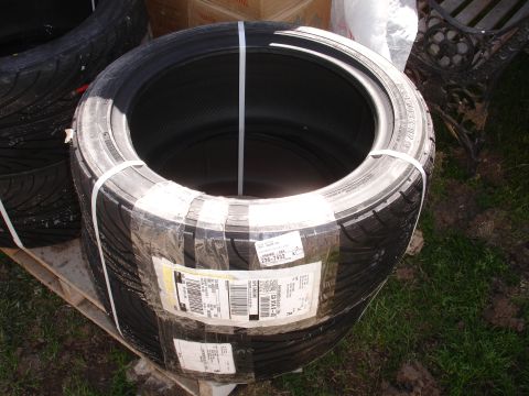 1995 Ford Taurus - Four tires are stacked and wrapped in plastic, secured with white straps. Shipping labels are visible on the packaging.