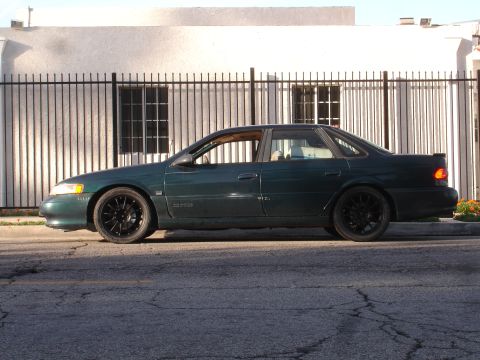 1995 Ford Taurus - Side profile of a dark green 1995 Ford Taurus sedan aftermarket black wheels.