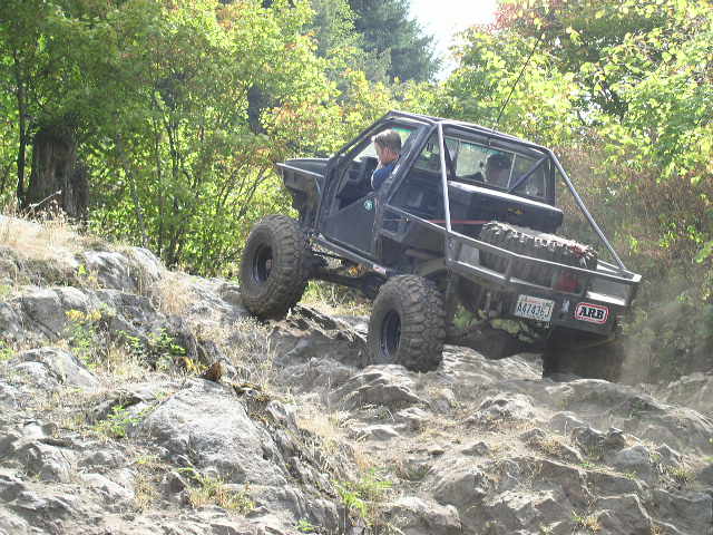 Doorless caged dark 4x4 with roll cage climbing rocks on a wooded trail