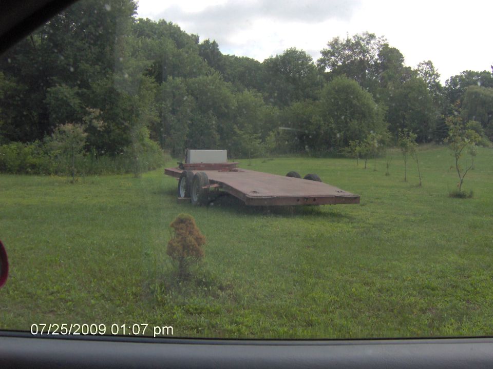 Flatbed trailer parked in a grassy field with trees in the background