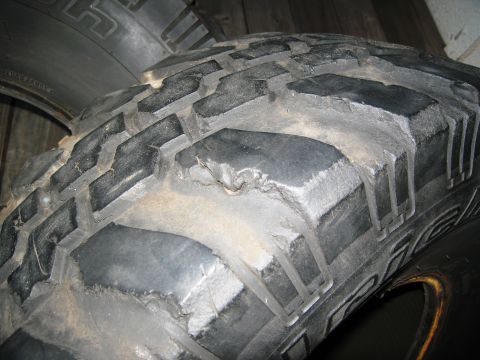 1986 Ford Bronco - This image shows a close-up view of a single, heavily used off-road tire with significant wear on its tread blocks.