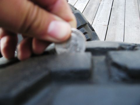 1986 Ford Bronco - A coin is used to check the tread depth of a tire, indicating wear.